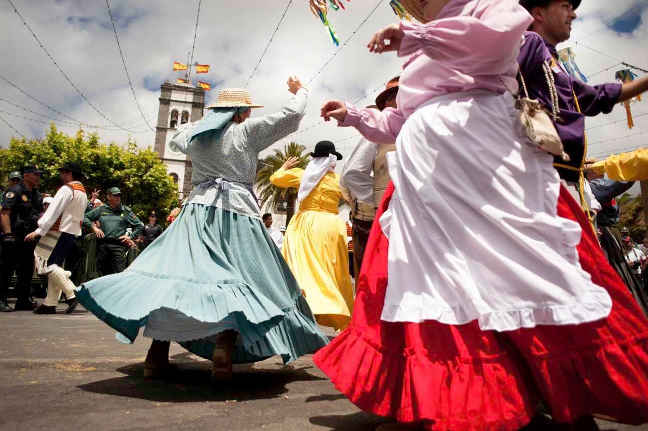 Grupo de personas bailando con vestimenta canaria típica y tradicional durante una romería en Tenerife, con faldas de colores y trajes populares en plena celebración.